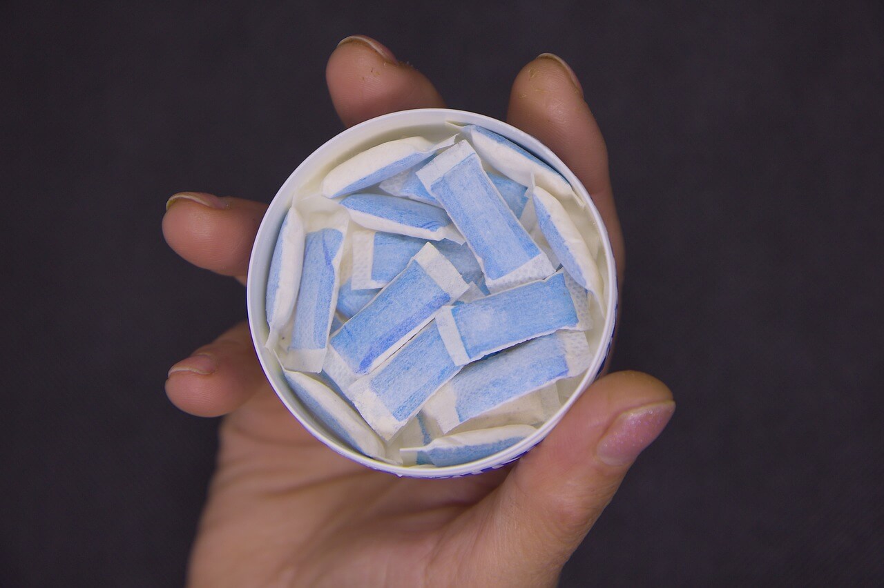 A few bags of snus on the palm of the hand with the pack in the background